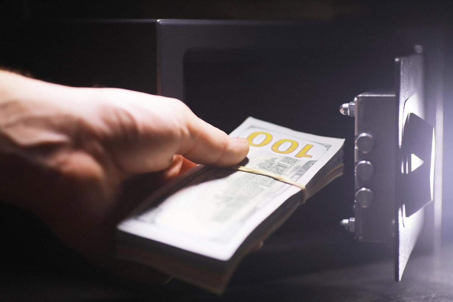 Hand placing a bundle of banknotes into a small home safe used to store cash and documents